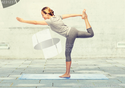 Image of woman making yoga in lord of the dance pose on mat