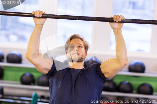 Image of man exercising on bar and doing pull-ups in gym