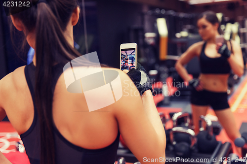 Image of woman with smartphone taking mirror selfie in gym