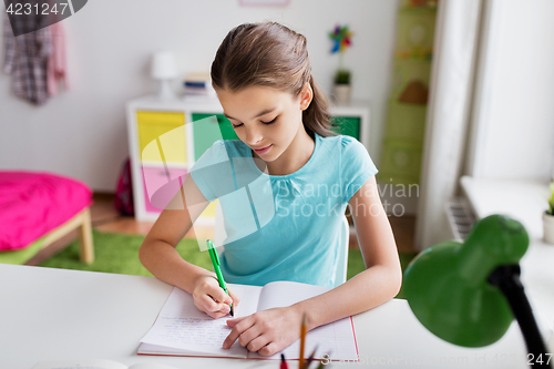 Image of happy girl writing to notebook at home