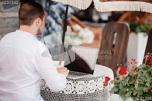 Image of Man working on laptop at the wooden table outdoors