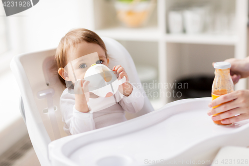 Image of baby drinking from spout cup in highchair at home