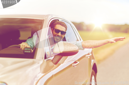 Image of happy man in shades driving car and waving hand