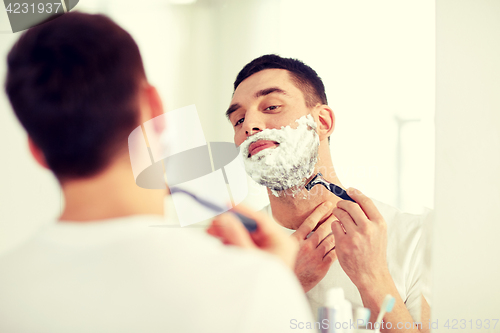 Image of man shaving beard with razor blade at bathroom