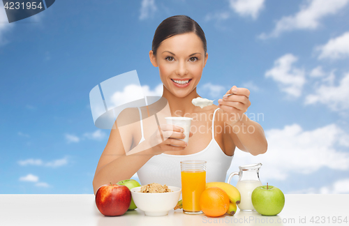 Image of happy woman with fruits, cereals eating yogurt