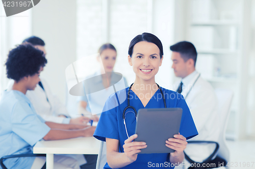 Image of happy doctor with tablet pc over team at clinic