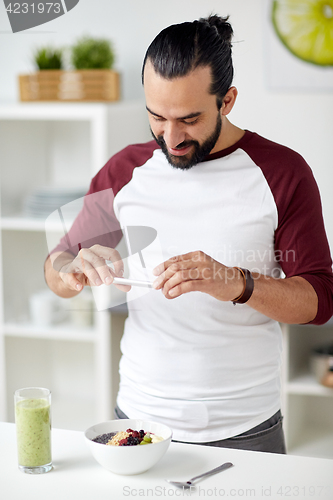 Image of man photographing breakfast by smartphone at home