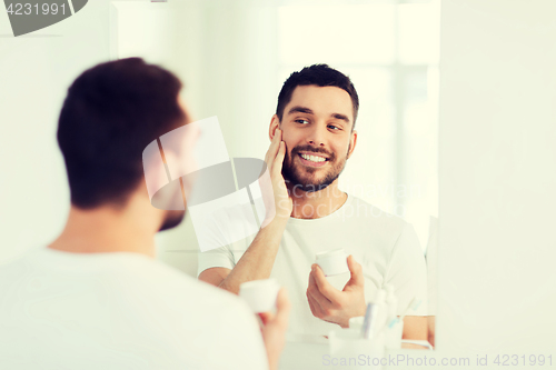 Image of happy young man applying cream to face at bathroom