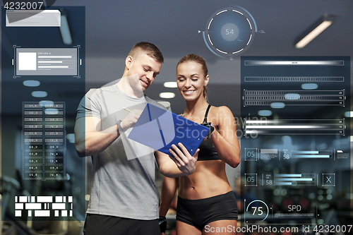 Image of smiling young woman with personal trainer in gym