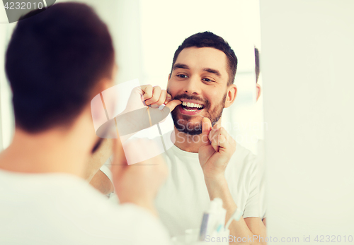 Image of man with dental floss cleaning teeth at bathroom