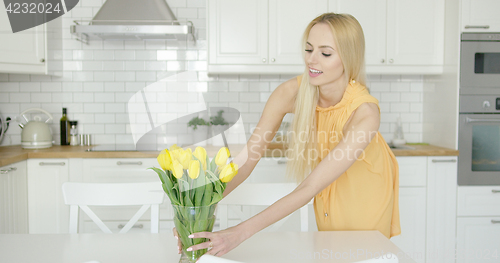 Image of Woman arranging vase with flowers on table