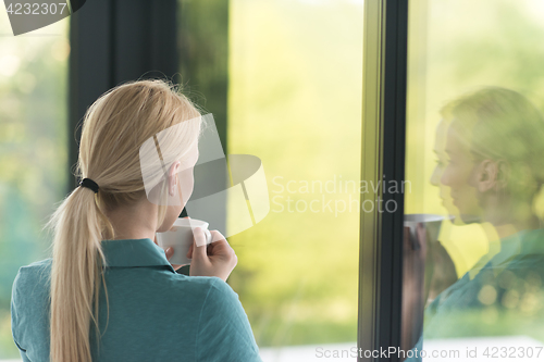 Image of young woman drinking morning coffee by the window