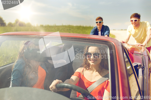 Image of happy friends pushing broken cabriolet car