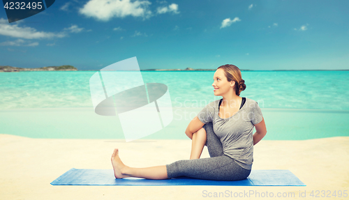 Image of woman making yoga in twist pose on mat over beach 