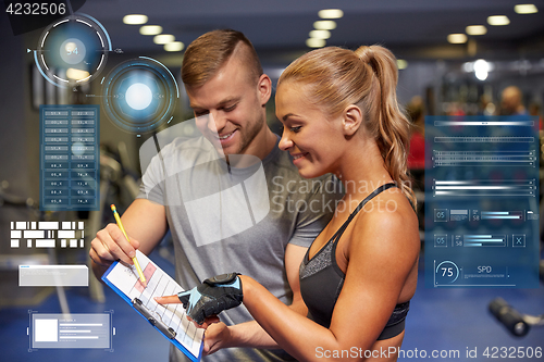 Image of smiling woman with trainer and clipboard in gym