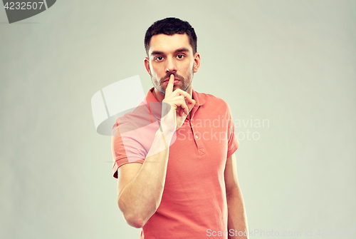 Image of young man making hush sign over gray background