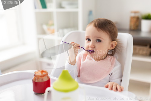 Image of baby girl with spoon eating puree from jar at home