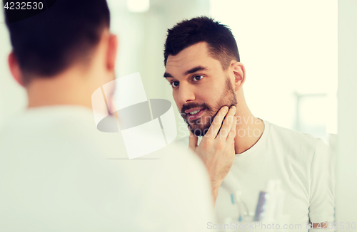 Image of happy young man looking to mirror at home bathroom