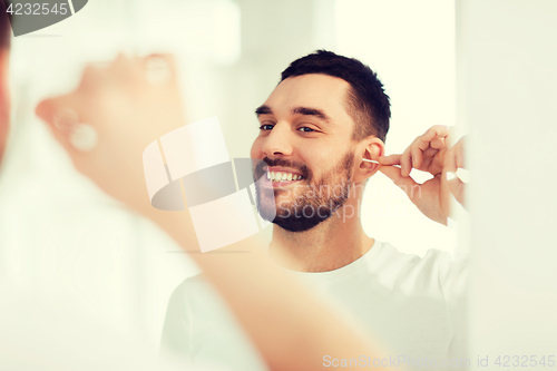 Image of man cleaning ear with cotton swab at bathroom