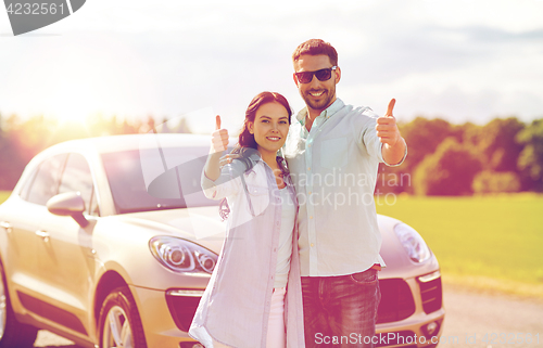Image of happy man and woman showing thumbs up at car