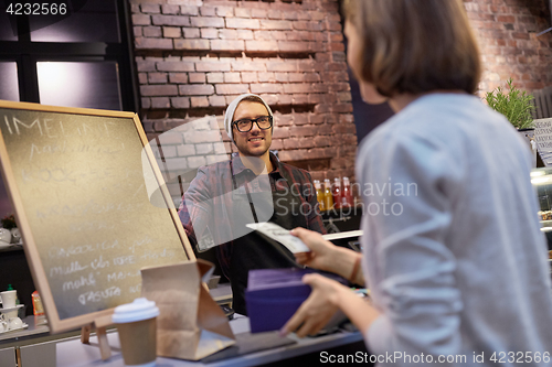 Image of happy barman and woman paying money at cafe