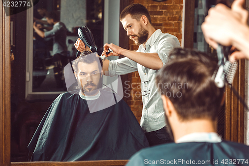 Image of Young handsome barber making haircut of attractive man in barbershop