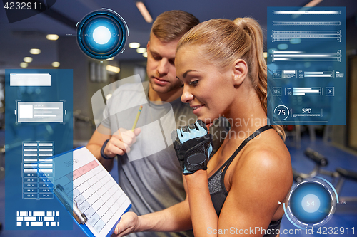 Image of smiling woman with trainer and clipboard in gym