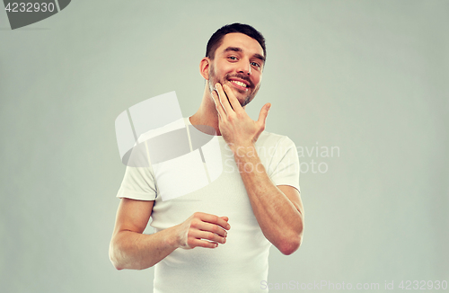 Image of happy young man applying cream or lotion to face