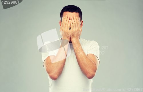 Image of man in white t-shirt covering his face with hands