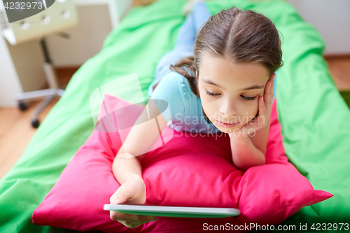 Image of smiling girl with tablet pc lying in bed at home