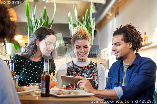 Image of friends with tablet pc, drinks and food at bar