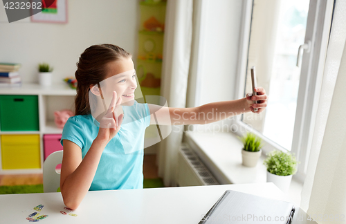 Image of happy girl with smartphone taking selfie at home