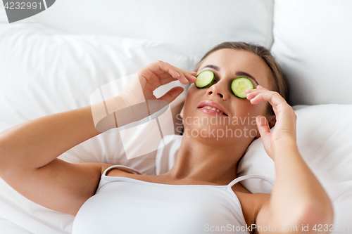 Image of beautiful woman applying cucumbers to face at home
