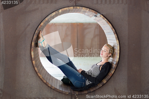 Image of Young thoughtful woman relaxing on bench in city park.