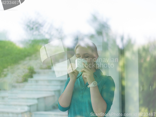 Image of young woman drinking morning coffee by the window