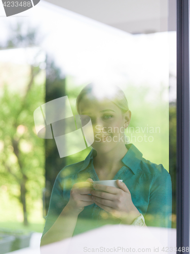 Image of young woman drinking morning coffee by the window