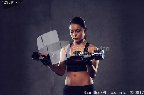 Image of young woman flexing muscles with dumbbells in gym