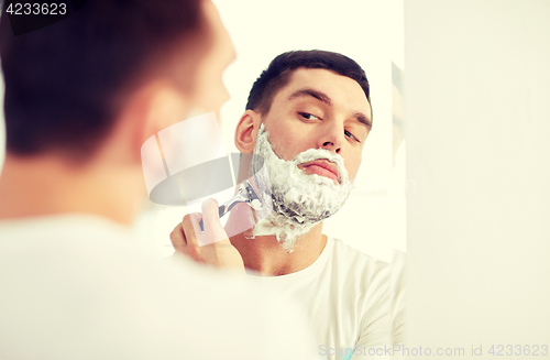 Image of man shaving beard with razor blade at bathroom