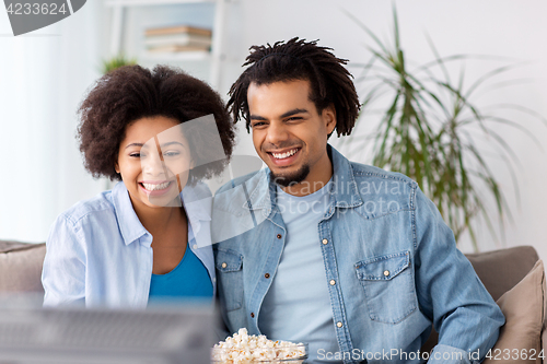 Image of smiling couple with popcorn watching tv at home
