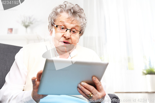 Image of Surprised elderly woman looks in the tablet screen