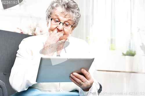 Image of University of the Third Age. Surprised elderly woman looks in the tablet screen Elderly woman surfs the internet.