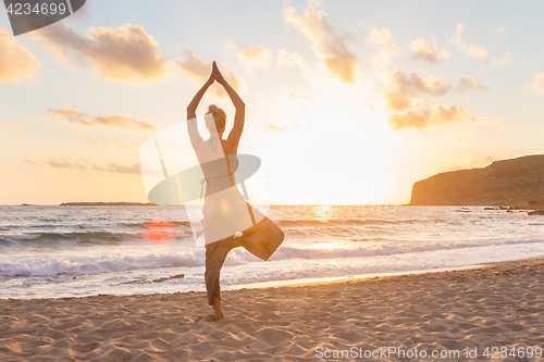 Image of Woman practicing yoga on sea beach at sunset.