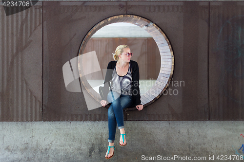 Image of Young thoughtful woman relaxing on bench in city park.