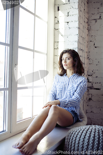 Image of young pretty brunette woman in her bedroom sitting at window, happy smiling lifestyle people concept 