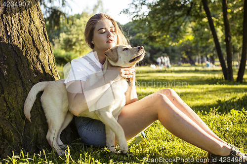 Image of young attractive blond woman playing with her dog in green park at summer, lifestyle people concept