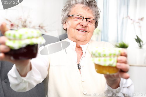 Image of A gift from her grandmother, colorful jam. Mature woman with personally prepared jars of jams. 