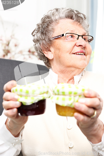 Image of A gift from her grandmother, colorful jam. Mature woman with personally prepared jars of jams. 