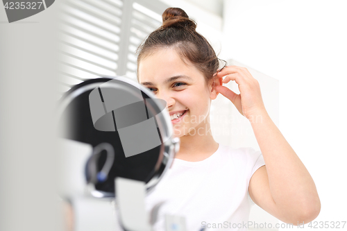 Image of Cheerful girl assumes hearing aid viewing in the mirror 