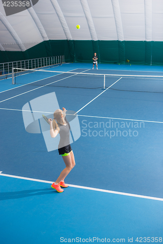 Image of The young girl in a closed tennis court with ball