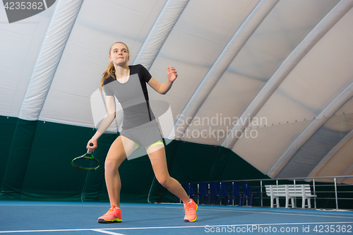 Image of The young girl in a closed tennis court with ball